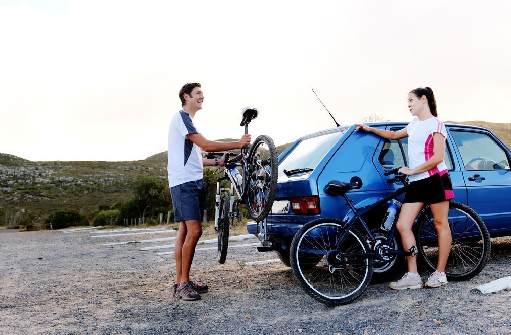 Panorama of a couple who have finished mountain biking outdoors and are loading the bicycles onto the car bike rack. large image, lots of copyspace, healthy lifestyle scene.